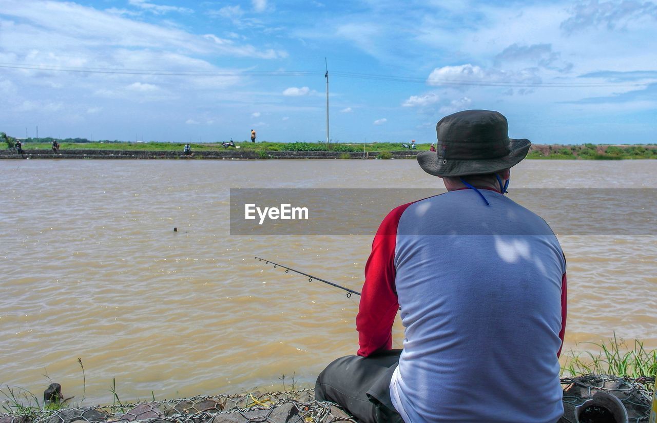 Rear view of man looking at river against sky