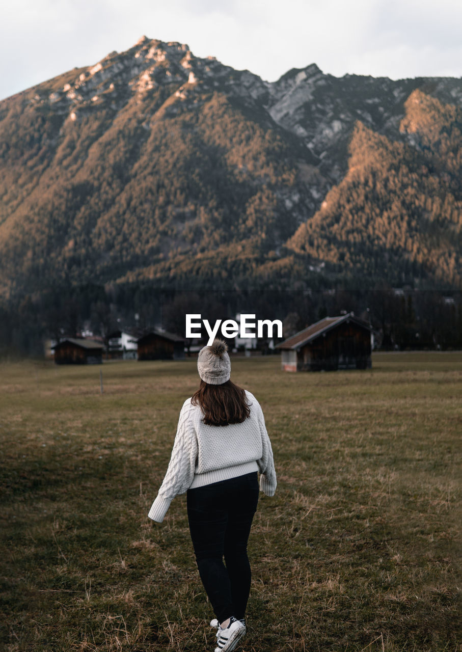 MAN STANDING ON FIELD AGAINST MOUNTAINS