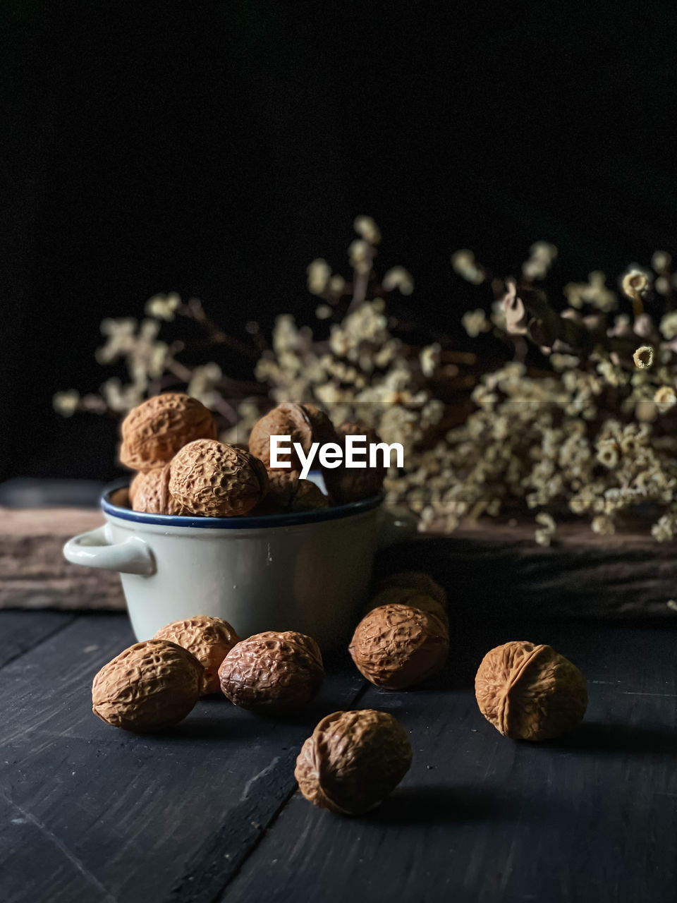 Roasted walnut in a ceramic bowl  with darker background and some dried flowers