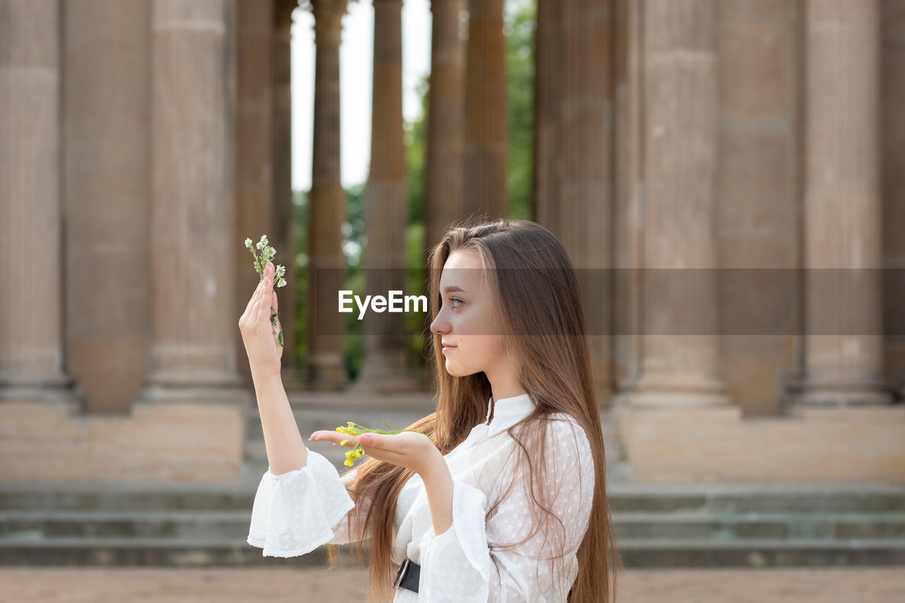 Close-up of young woman holding flower standing against columns