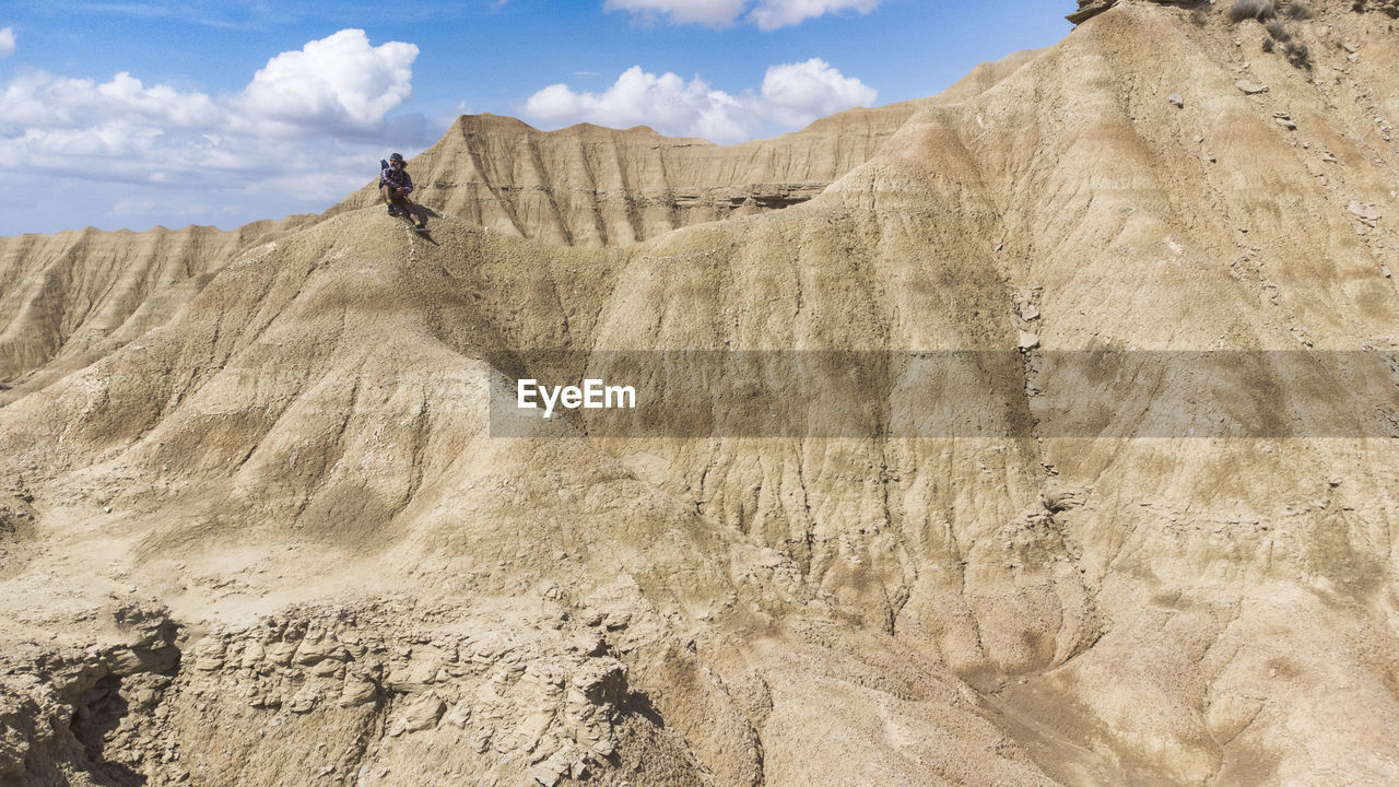 The man is sitting on top of the rocky dunes and enjoying the desert landscape.