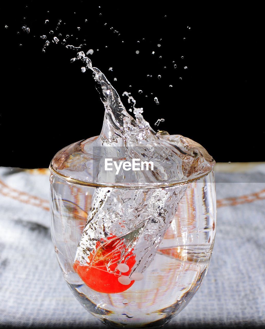 Close-up of water splashing in drinking glass on table against black background