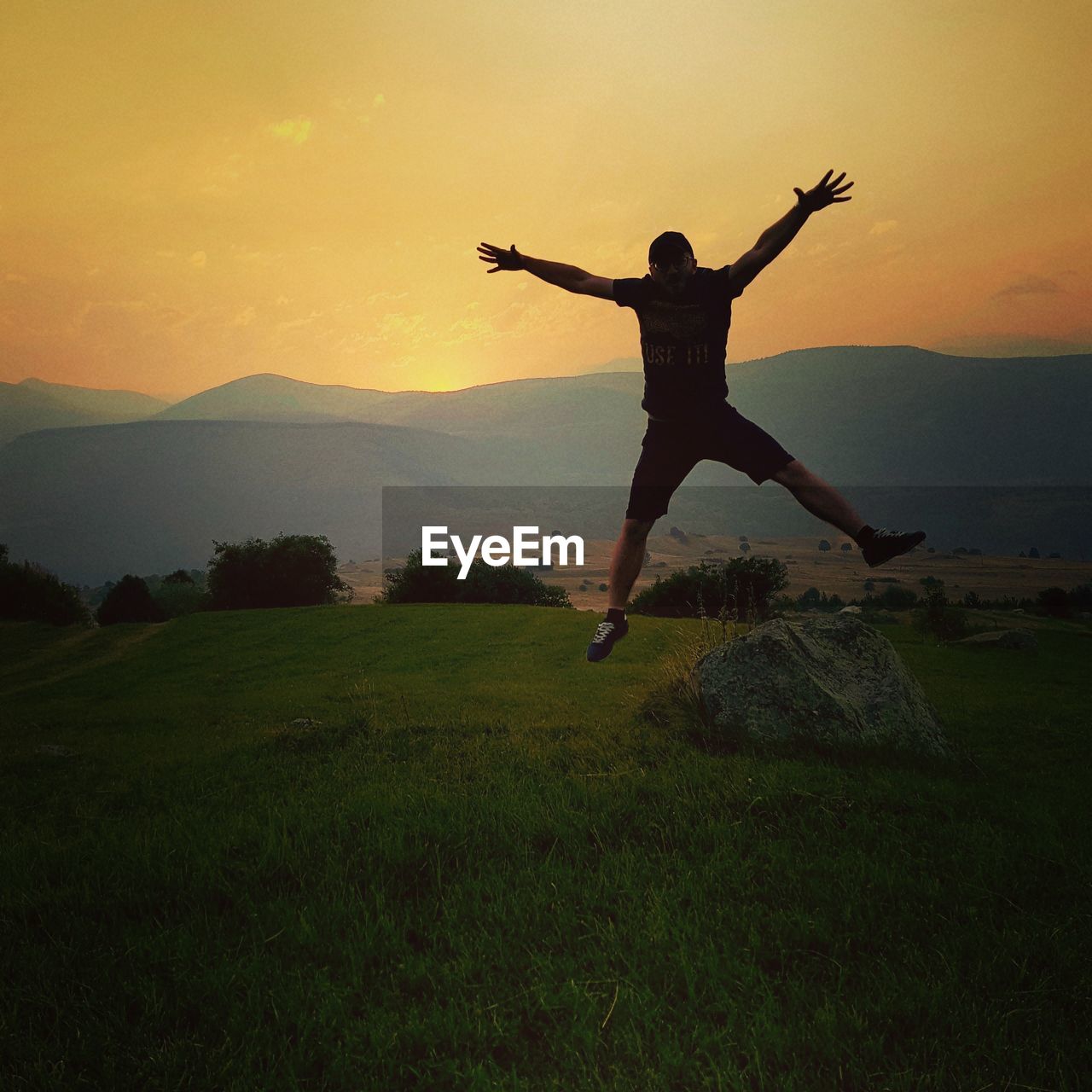 Full length of man jumping on land against mountains and sky during sunset