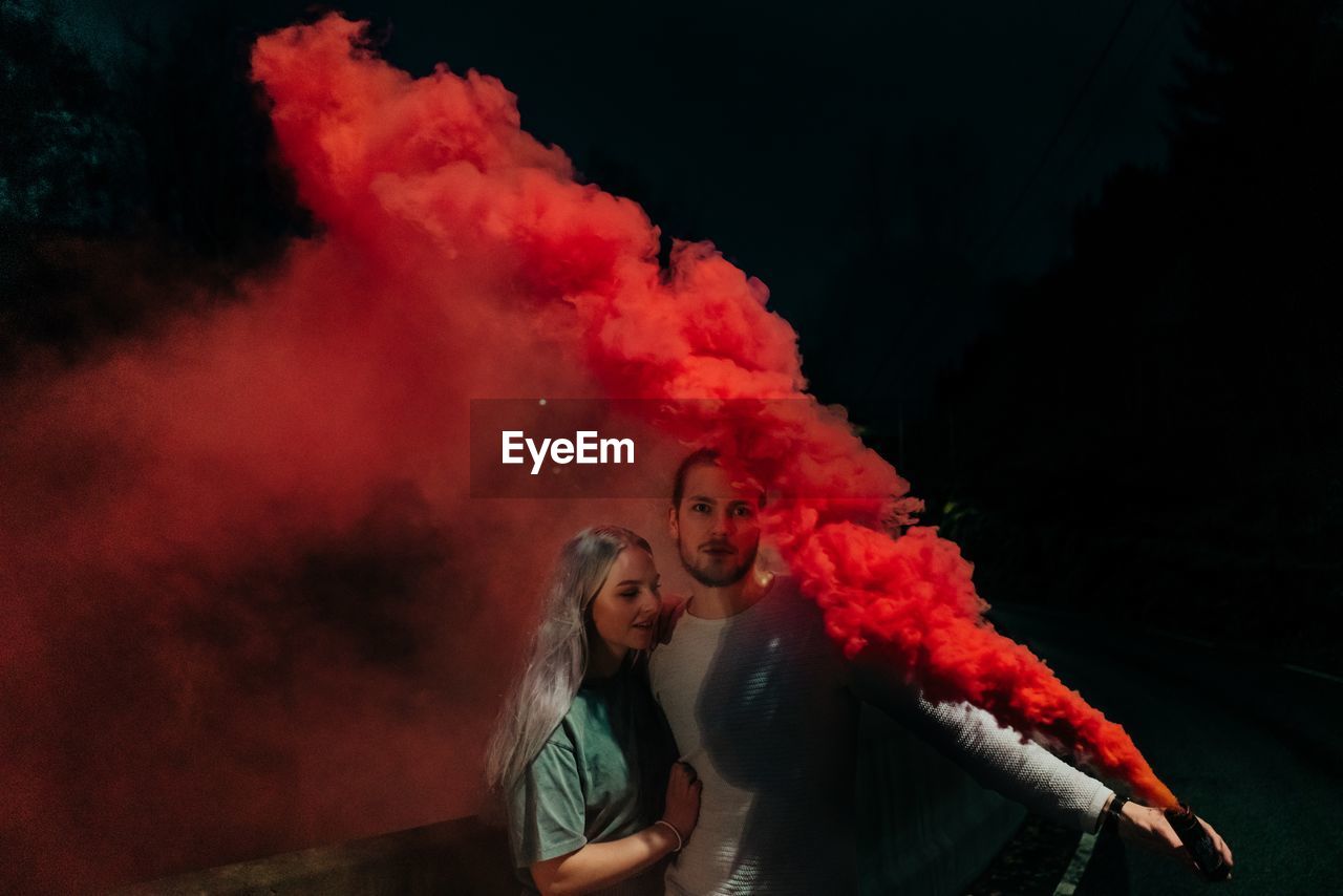 Man embracing woman while holding distress flare at night