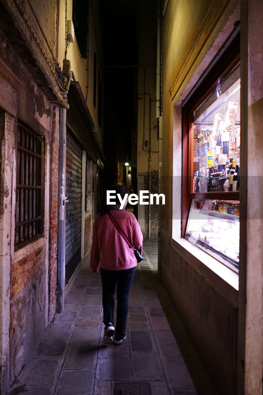 REAR VIEW OF MAN WALKING ON CORRIDOR