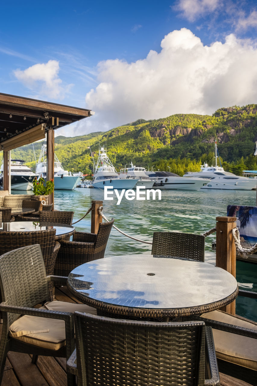 Chairs and tables at restaurant by sea by eden island, seychelles, against sky