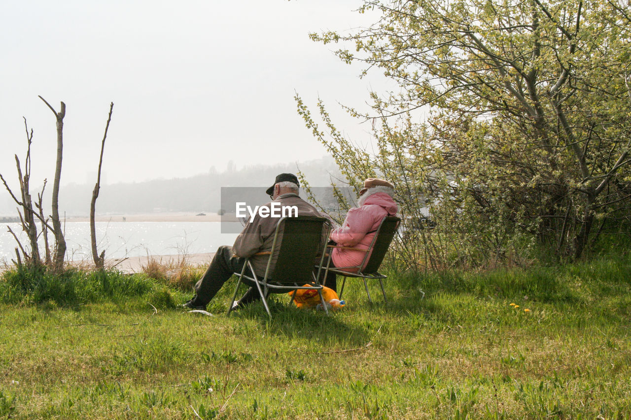 PEOPLE SITTING ON GRASS AGAINST TREES