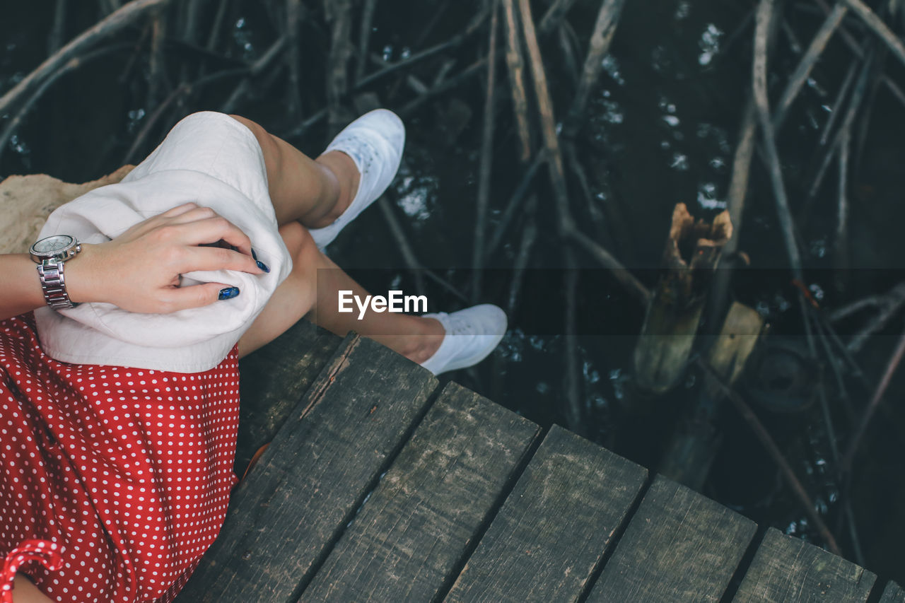 Low section of woman sitting on pier over lake