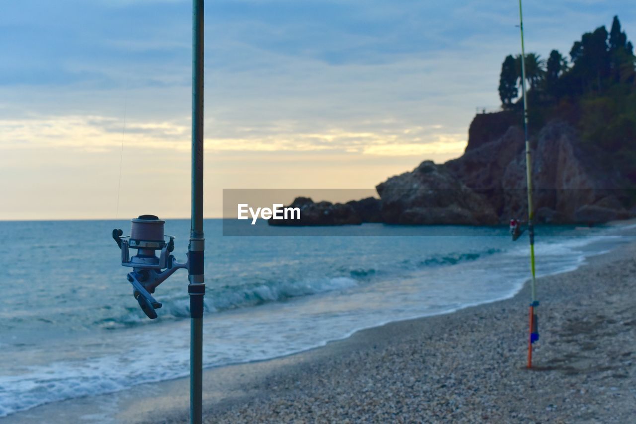 Fishing rods at beach against sky during sunset