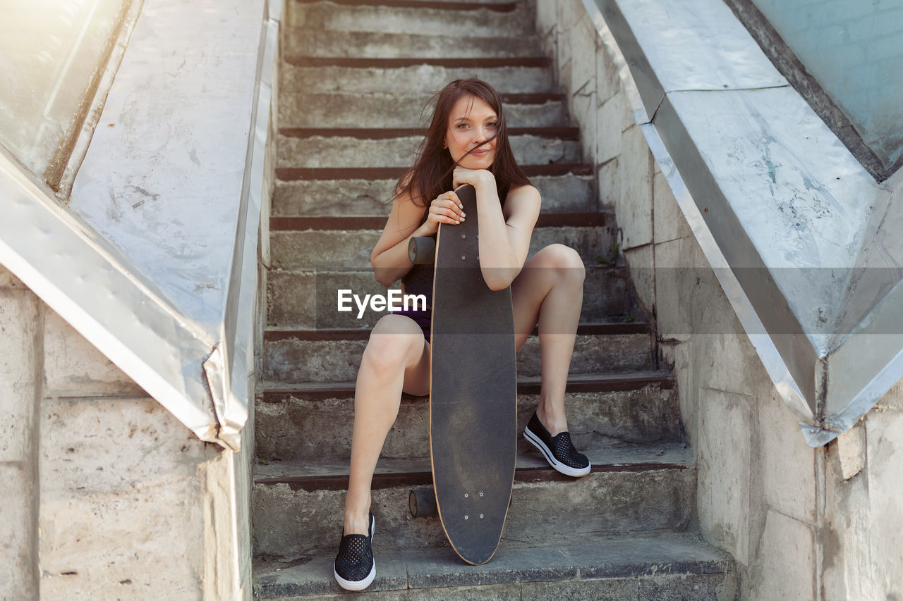 Portrait of smiling young woman with skateboard sitting by steps