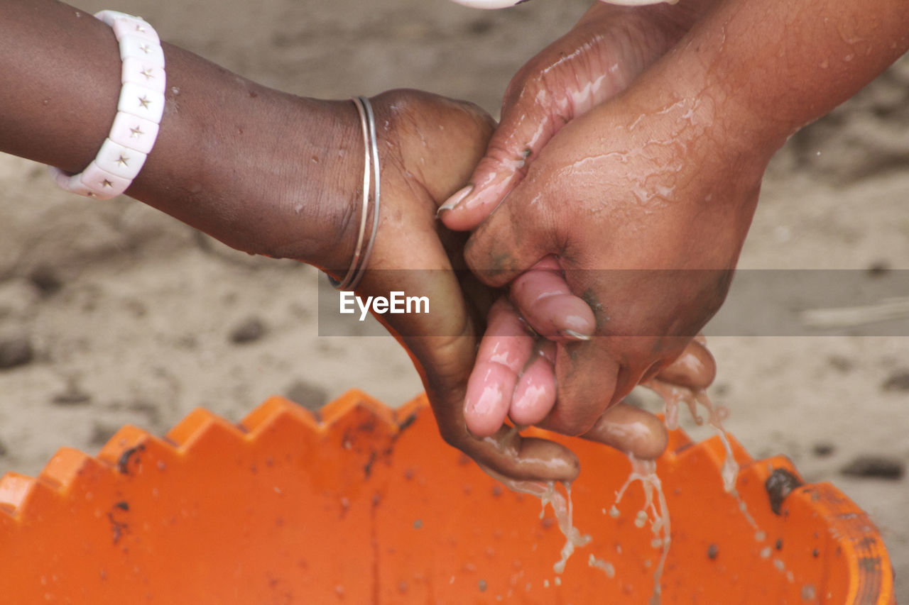 Cropped image of friends washing hands over bucket at beach