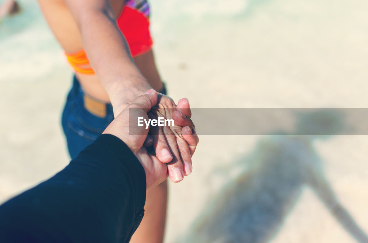 Cropped image of boyfriend holding girlfriend hand at beach