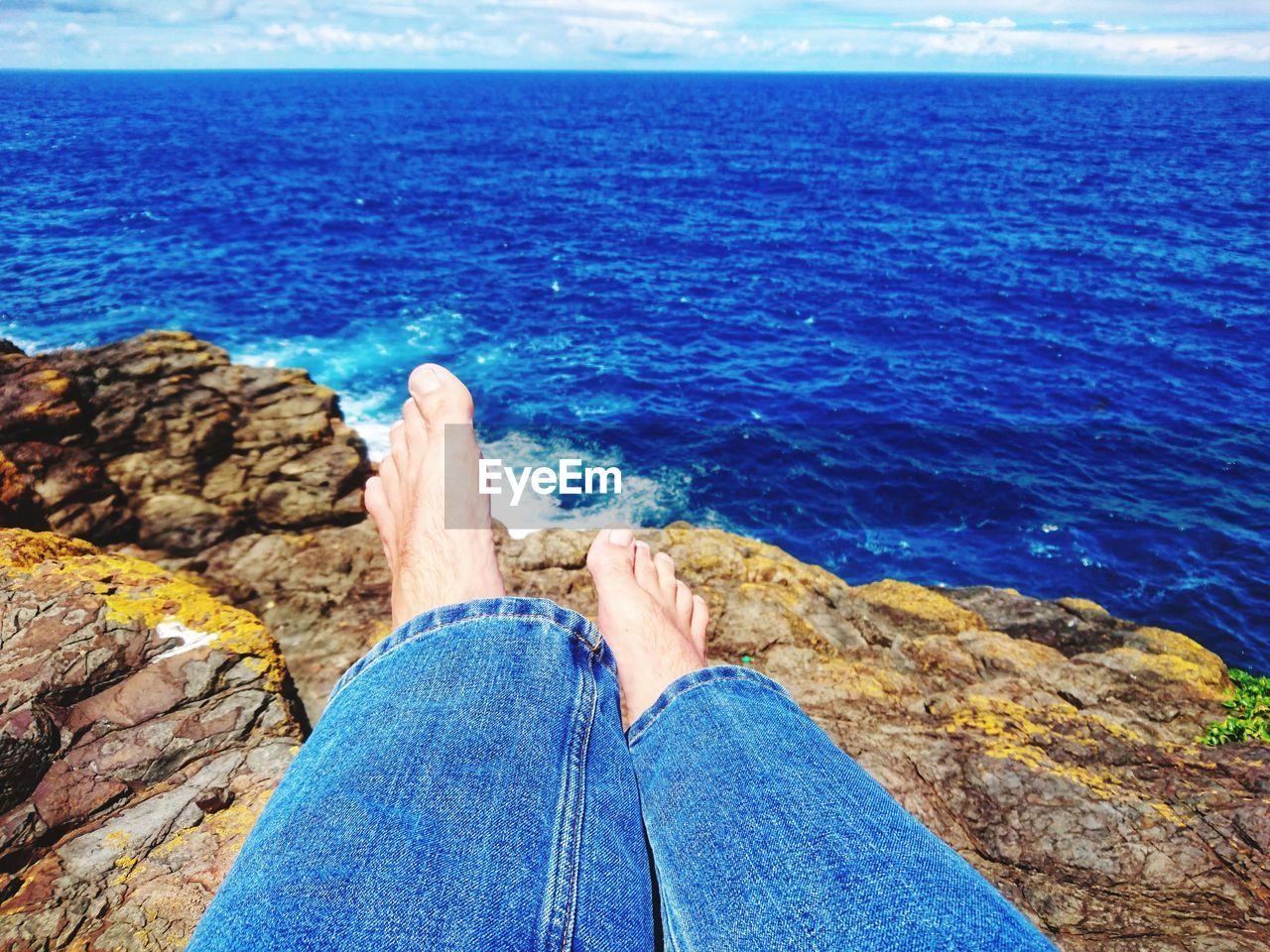 LOW SECTION OF MAN ON ROCK BY SEA