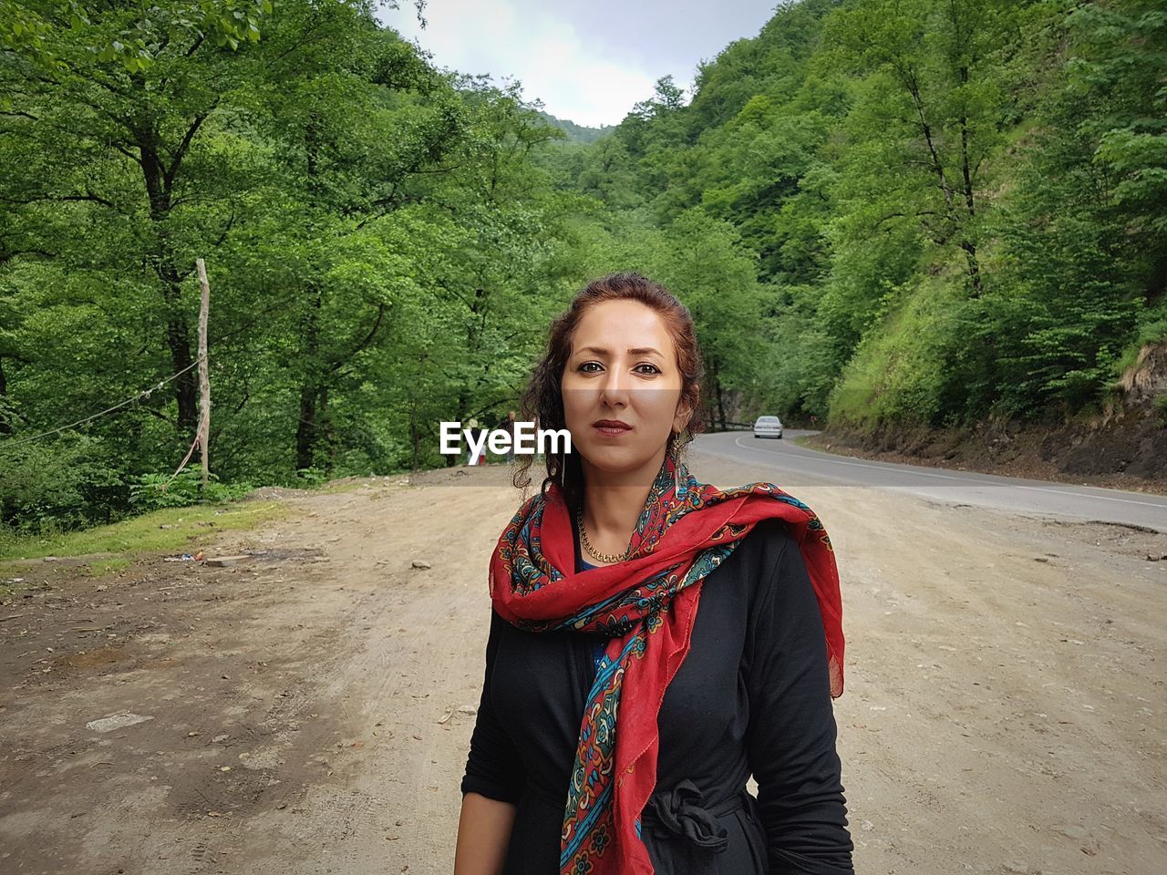 Portrait of beautiful young woman standing at roadside against trees