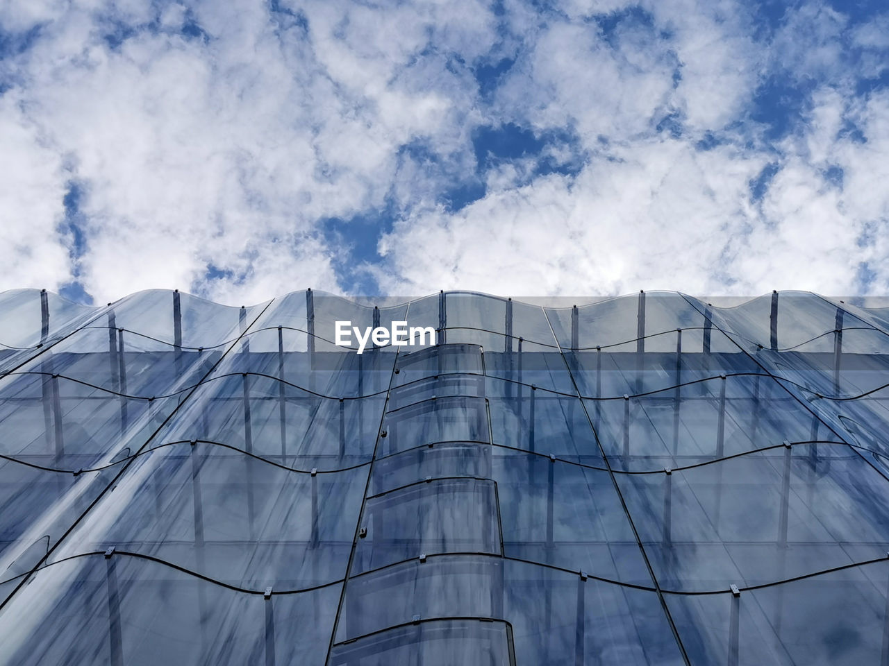 Low angle view of modern building against sky with wavy glass facade