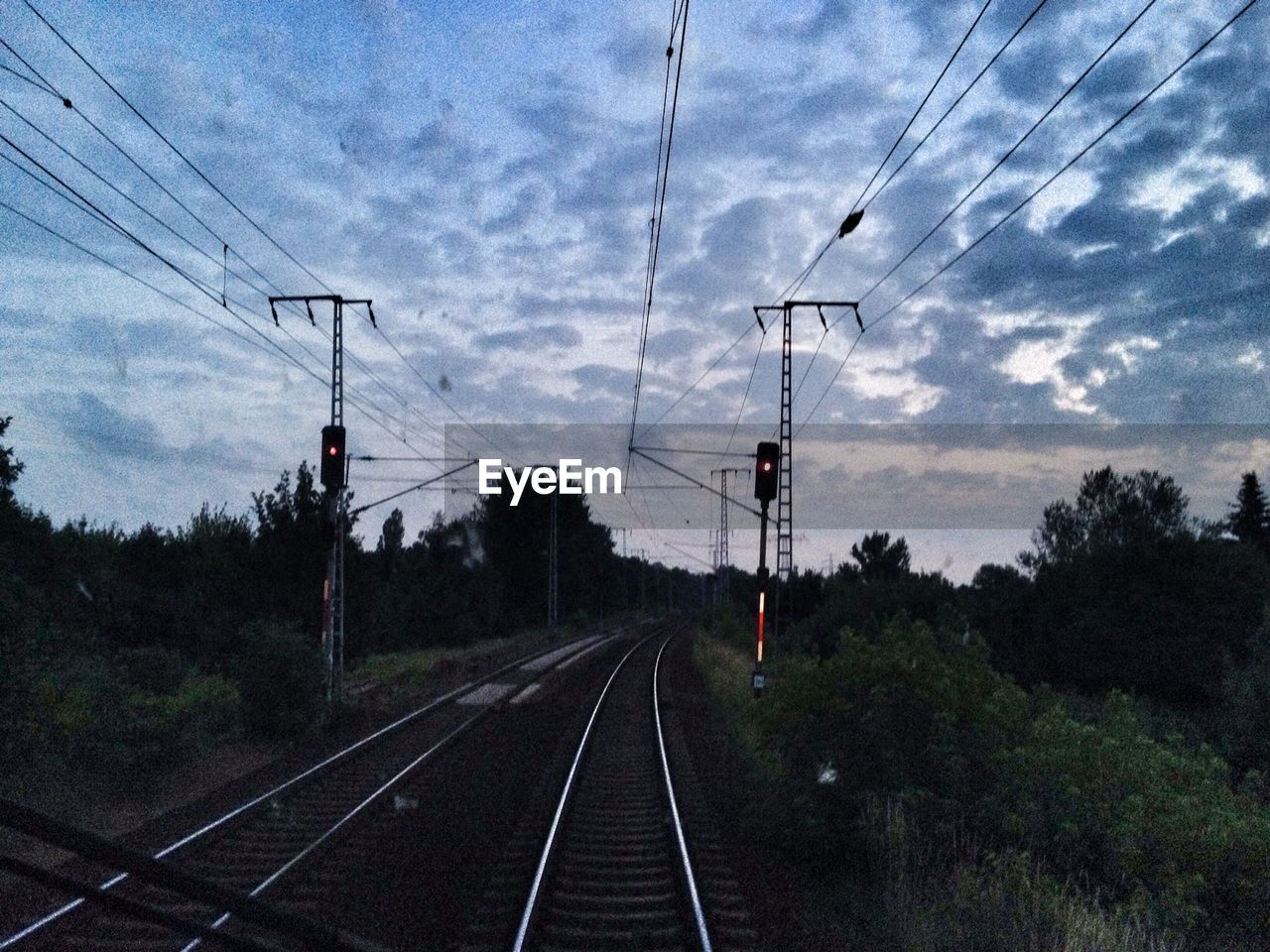 Railway tracks and electricity pylons against cloudy sky at dusk