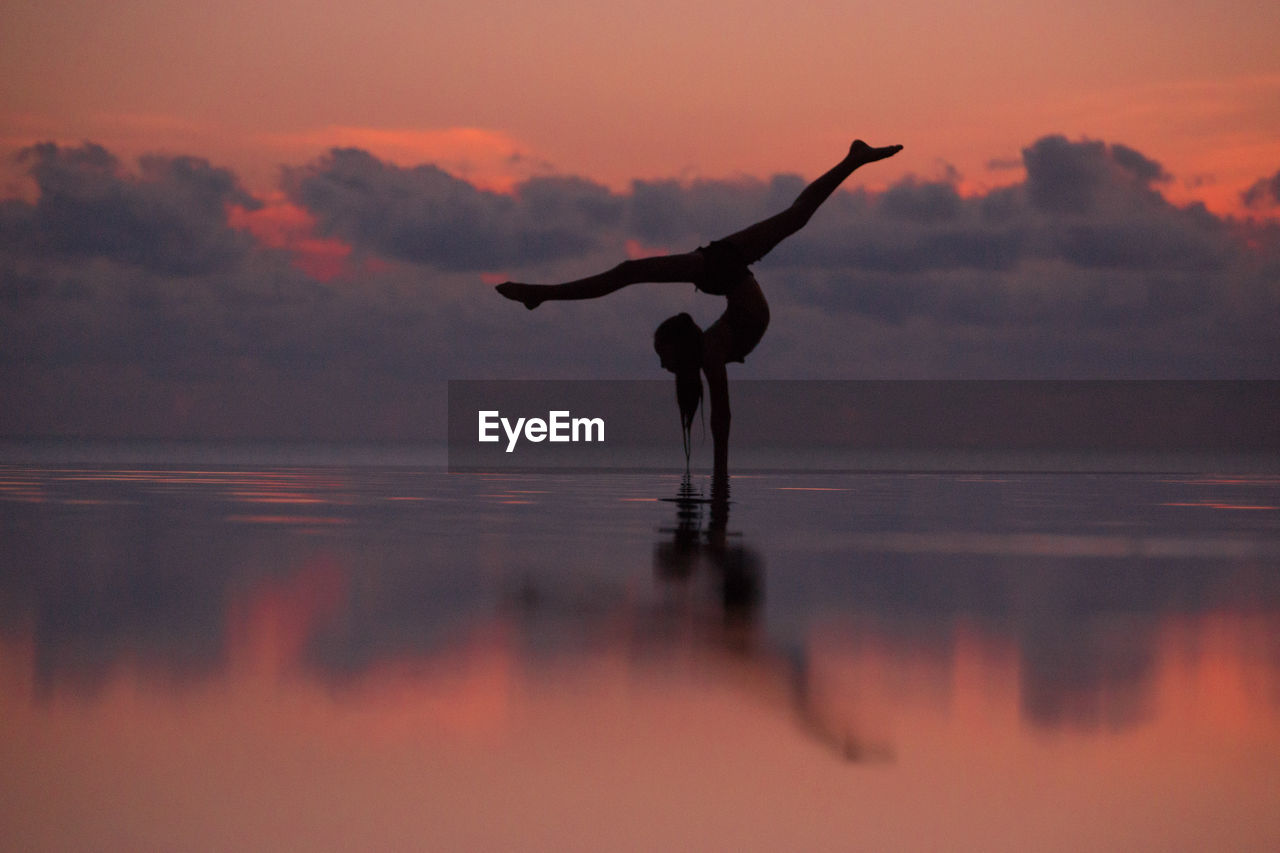 Full length of woman doing ballet dancing in infinity pool by sea against sky