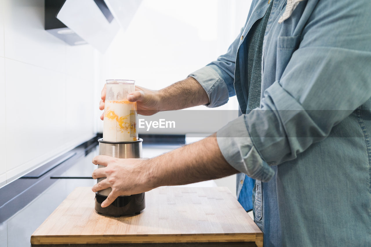 Man cooking in the kitchen in a denim shirt. an anonymous is going to beat a mixture of flour, eggs and milk