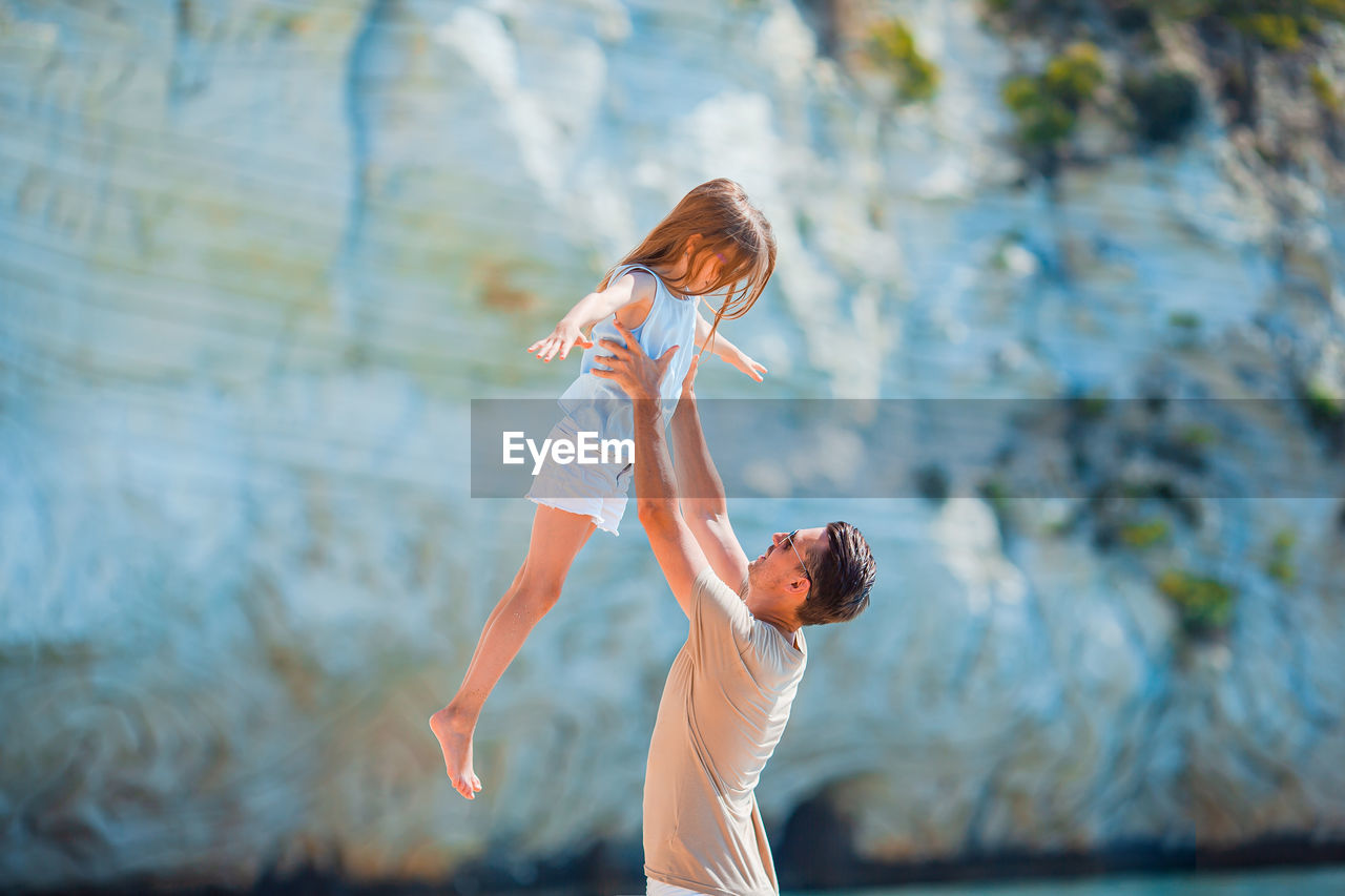 Side view of father holding daughter midair
