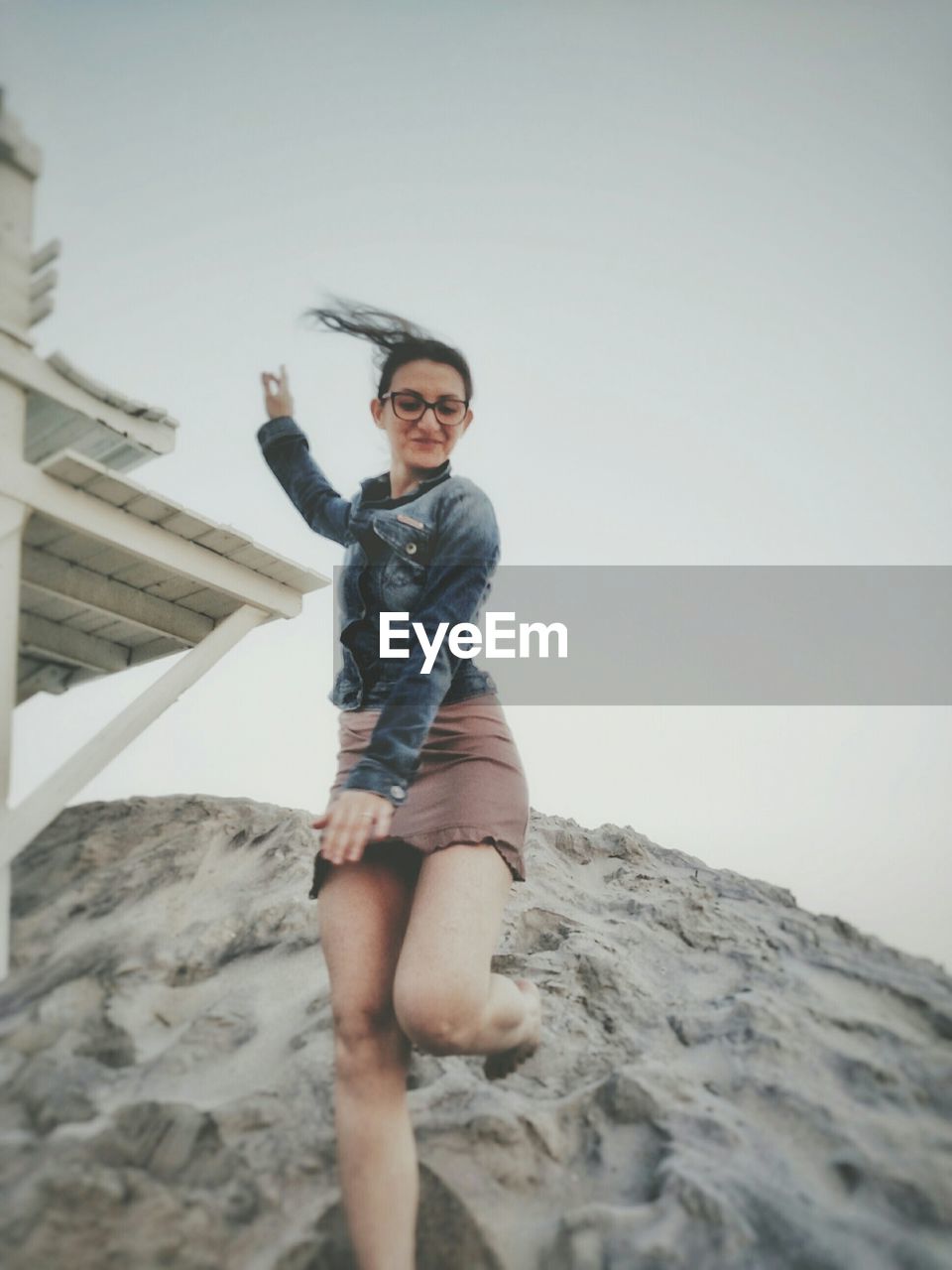 Low angle view of happy young woman standing on rock against sky