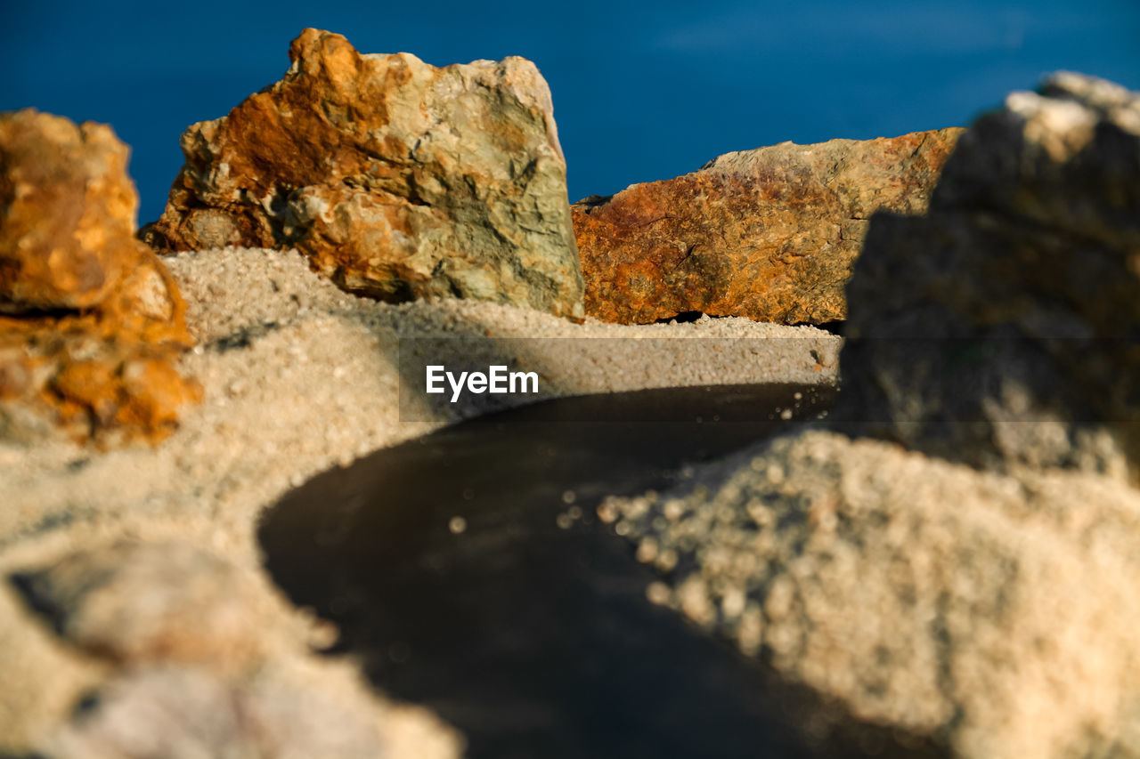 rock, nature, sky, sea, land, water, no people, rock formation, sunlight, geology, scenics - nature, environment, travel destinations, beauty in nature, landscape, travel, outdoors, reflection, terrain, mountain, coast, day, sand, tranquility, macro photography, blue, sunny, beach