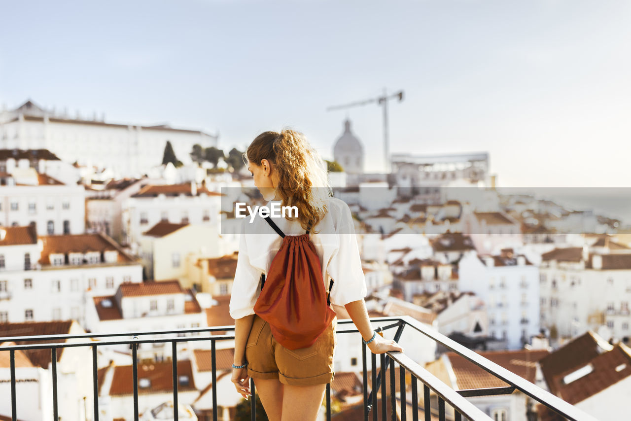 Rear view of woman standing by railing against buildings and sky