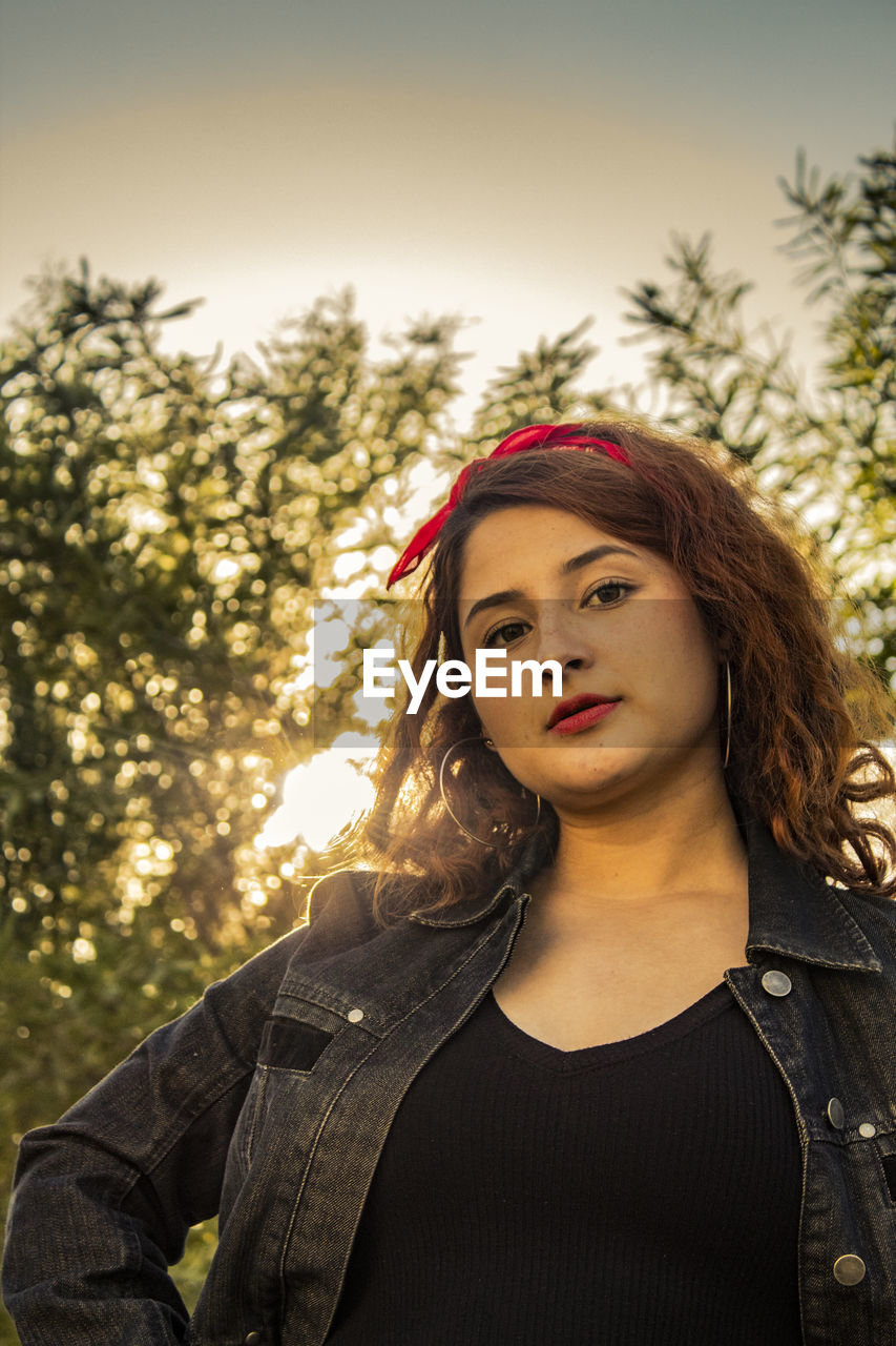 Portrait of beautiful woman standing against tree during sunset