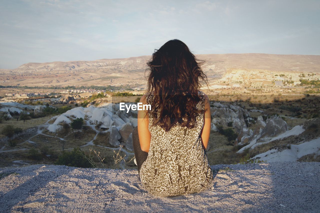 Rear view of woman sitting on mountain against sky