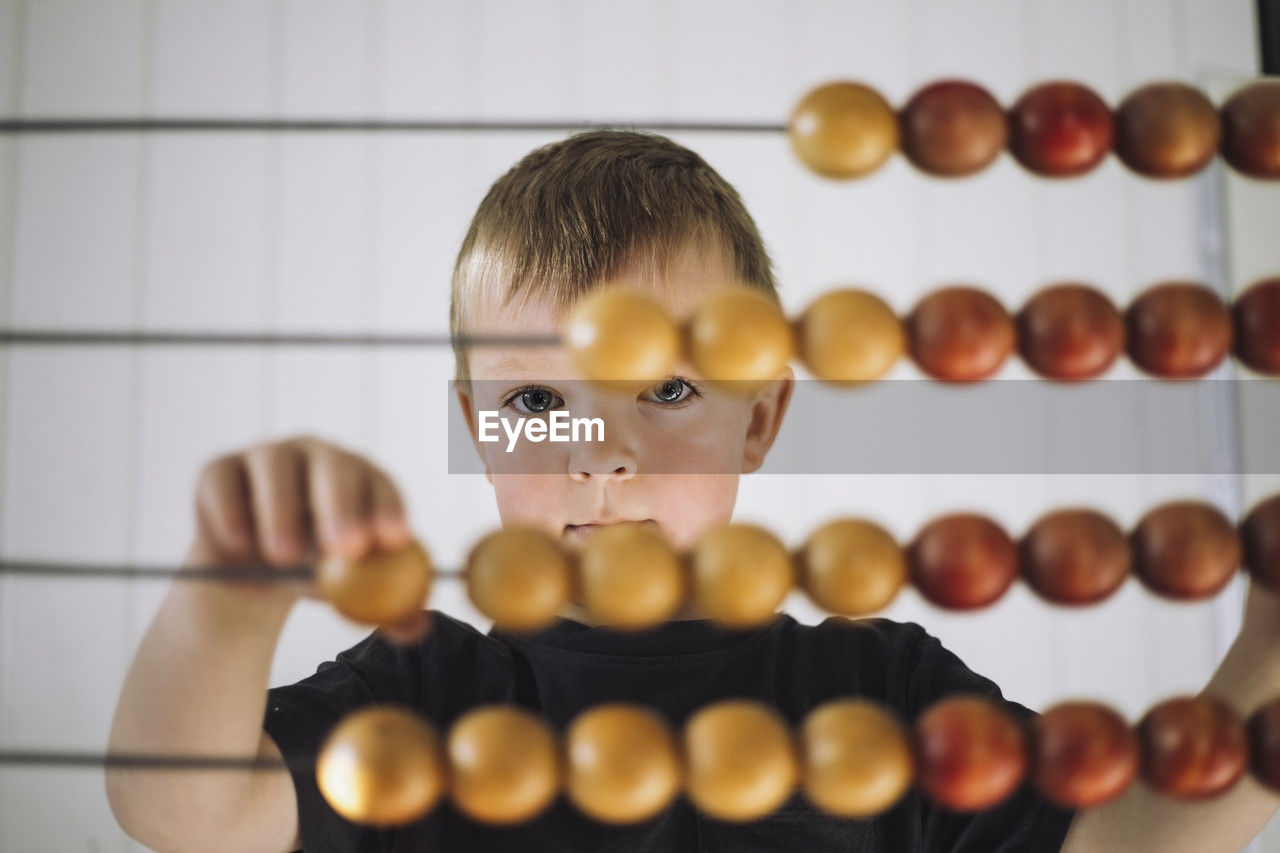 Portrait of schoolboy using abacus to count in classroom at kindergarten