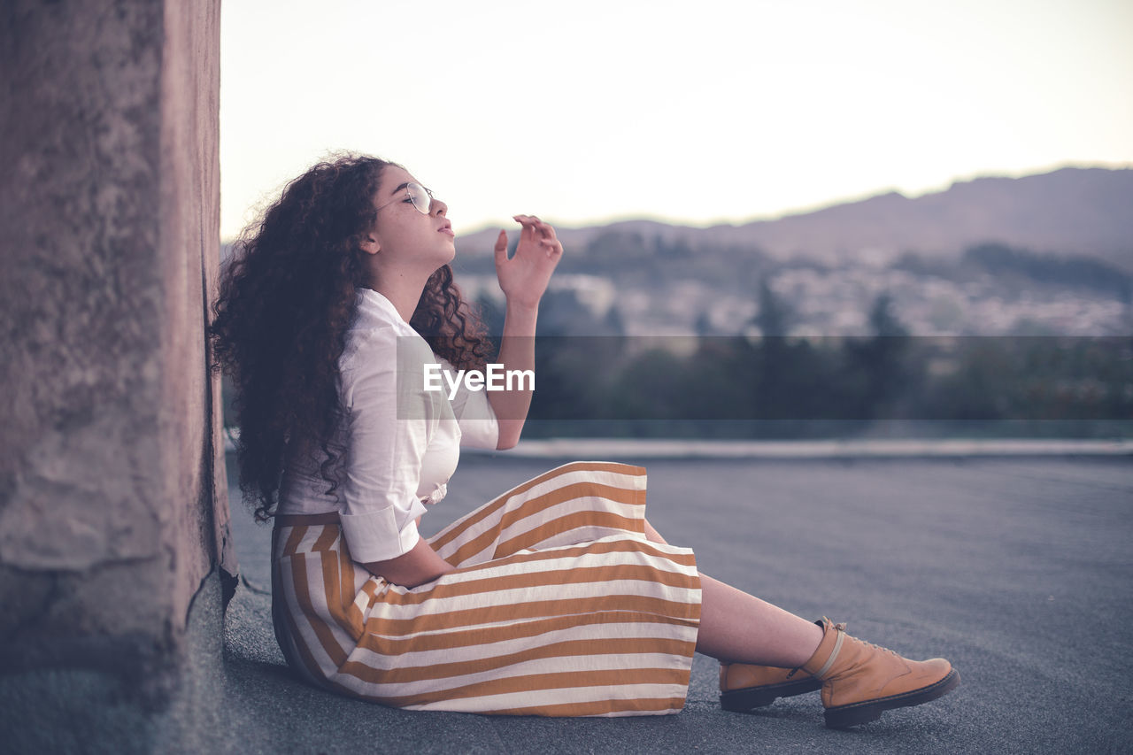 Young woman with curly hair looking away while sitting outdoors 