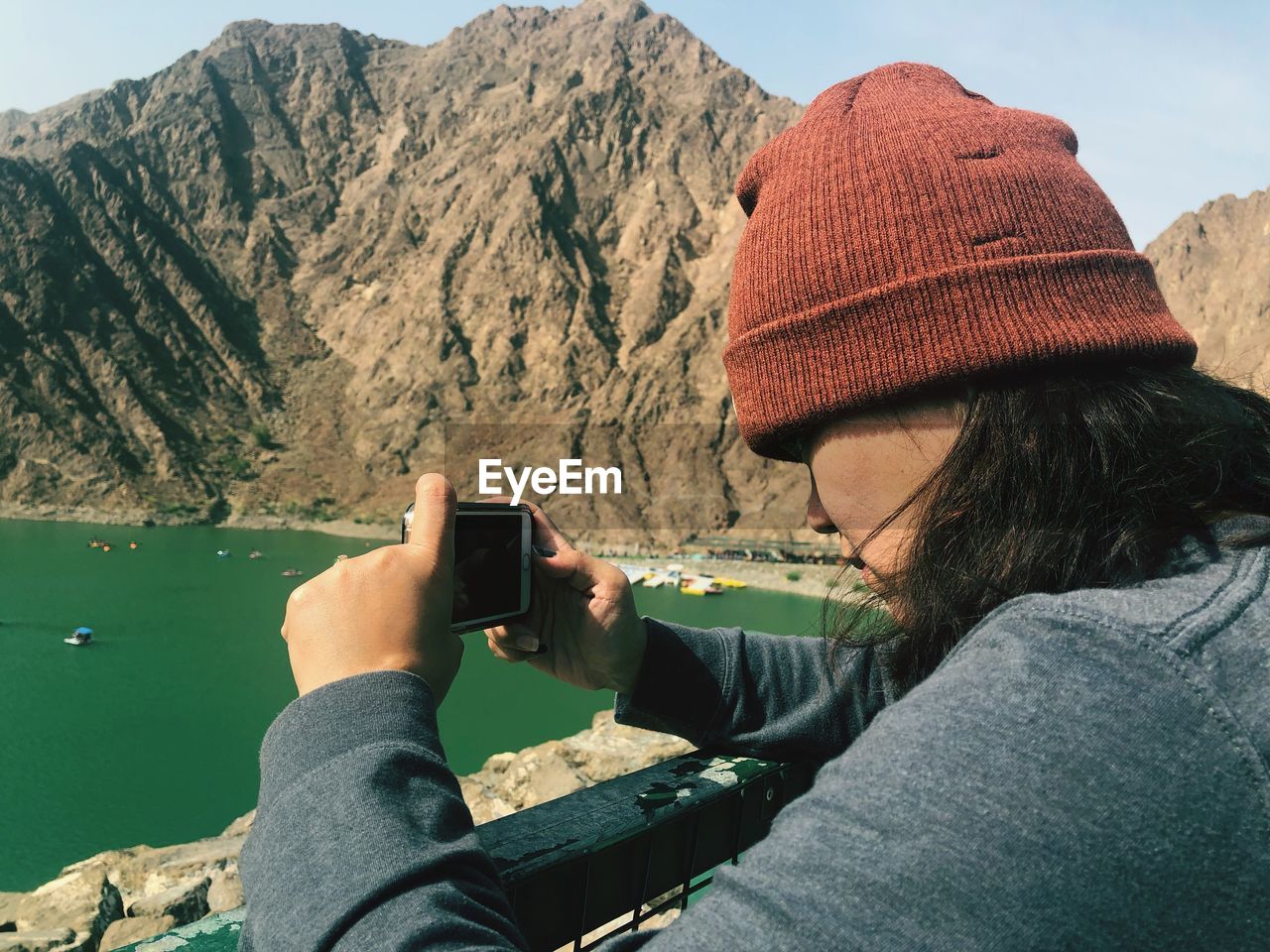 Side view of woman photographing with mobile phone against mountains