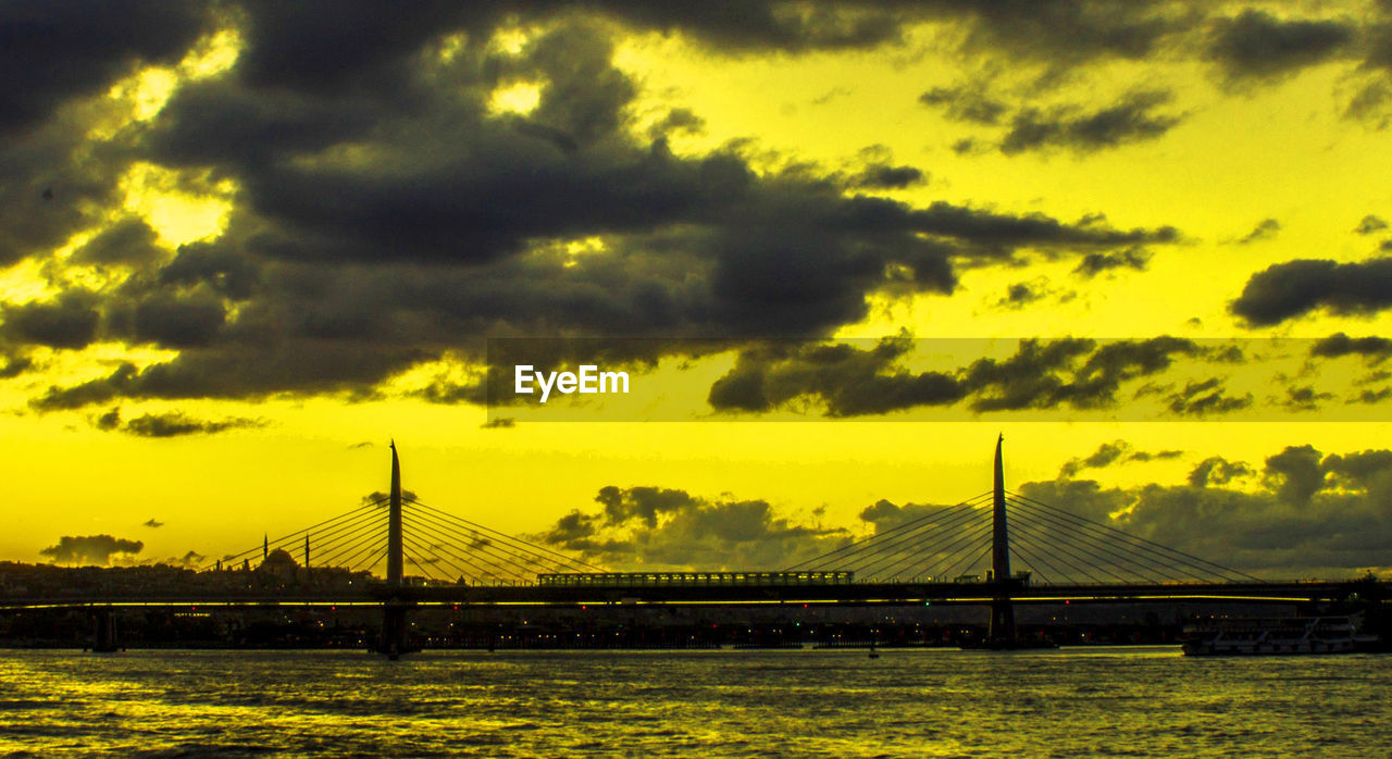 Cable-stayed bridge in river against yellow sky