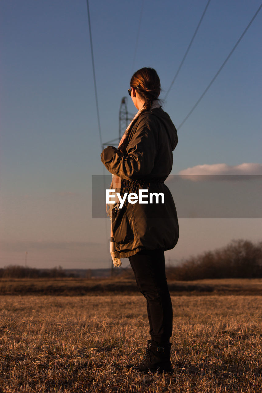 Full length side view of woman standing on land against sky during sunset