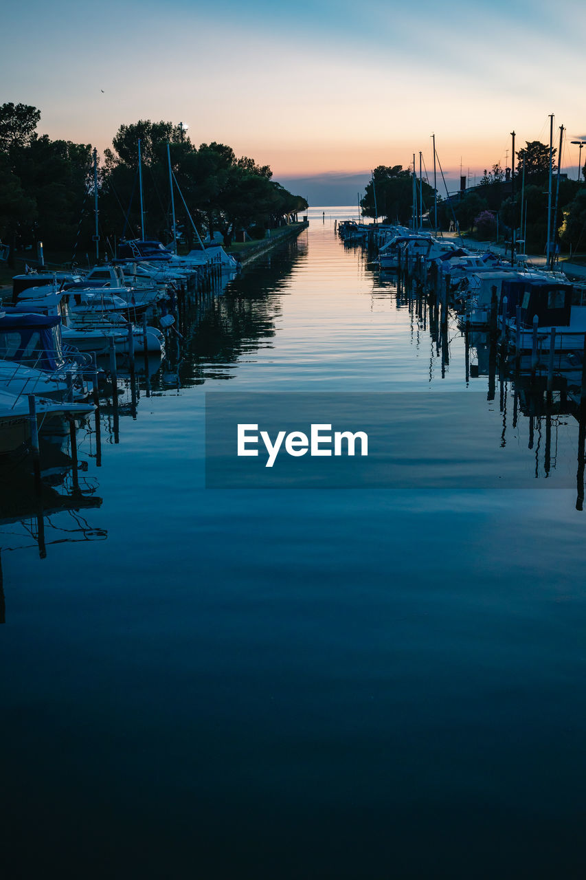 Boats moored in harbor at sunset