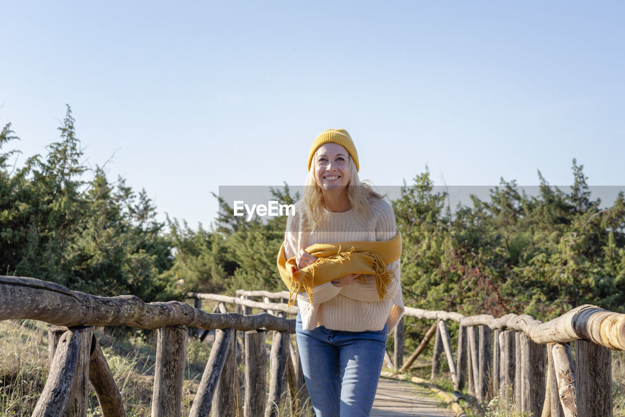 Smiling woman with scarf standing on wooden bridge