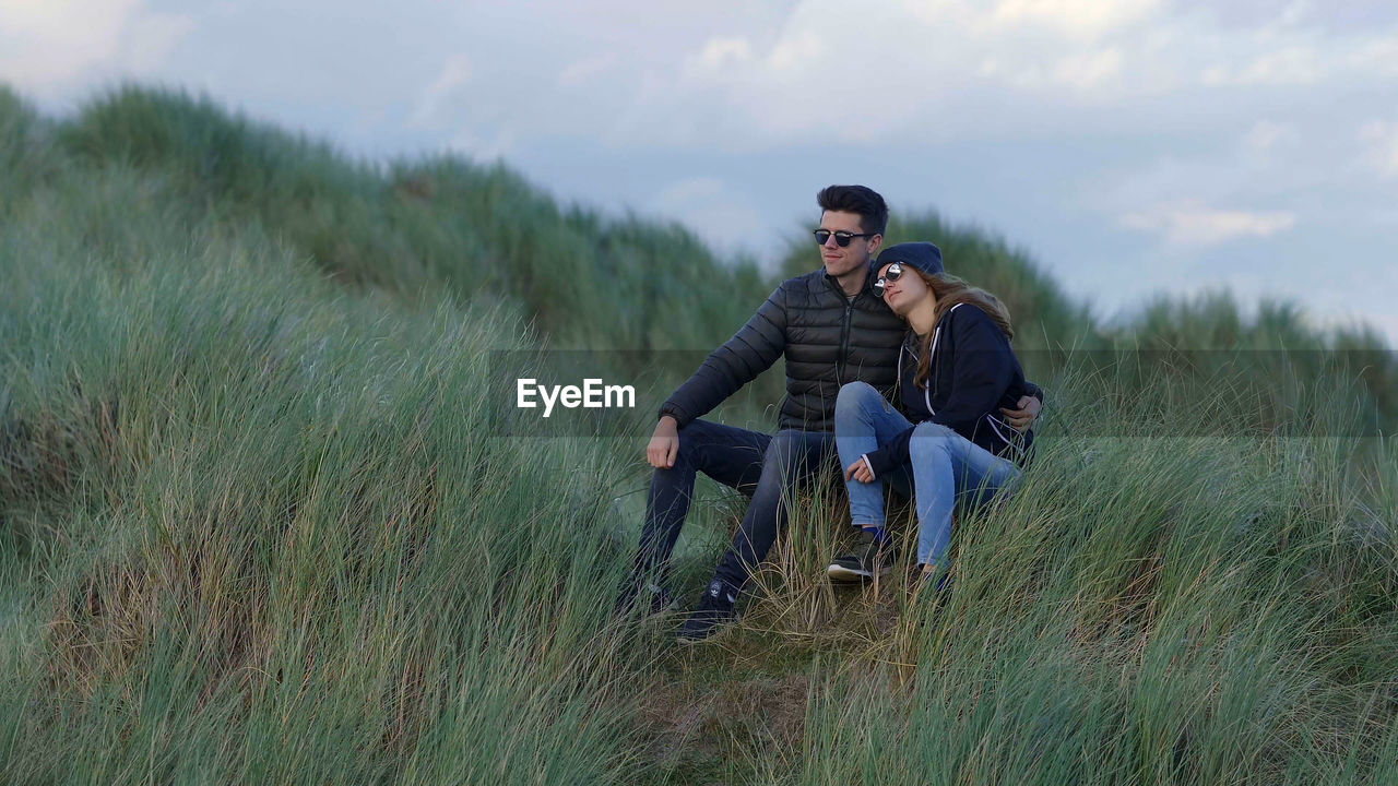 YOUNG COUPLE SITTING ON LAND IN FIELD