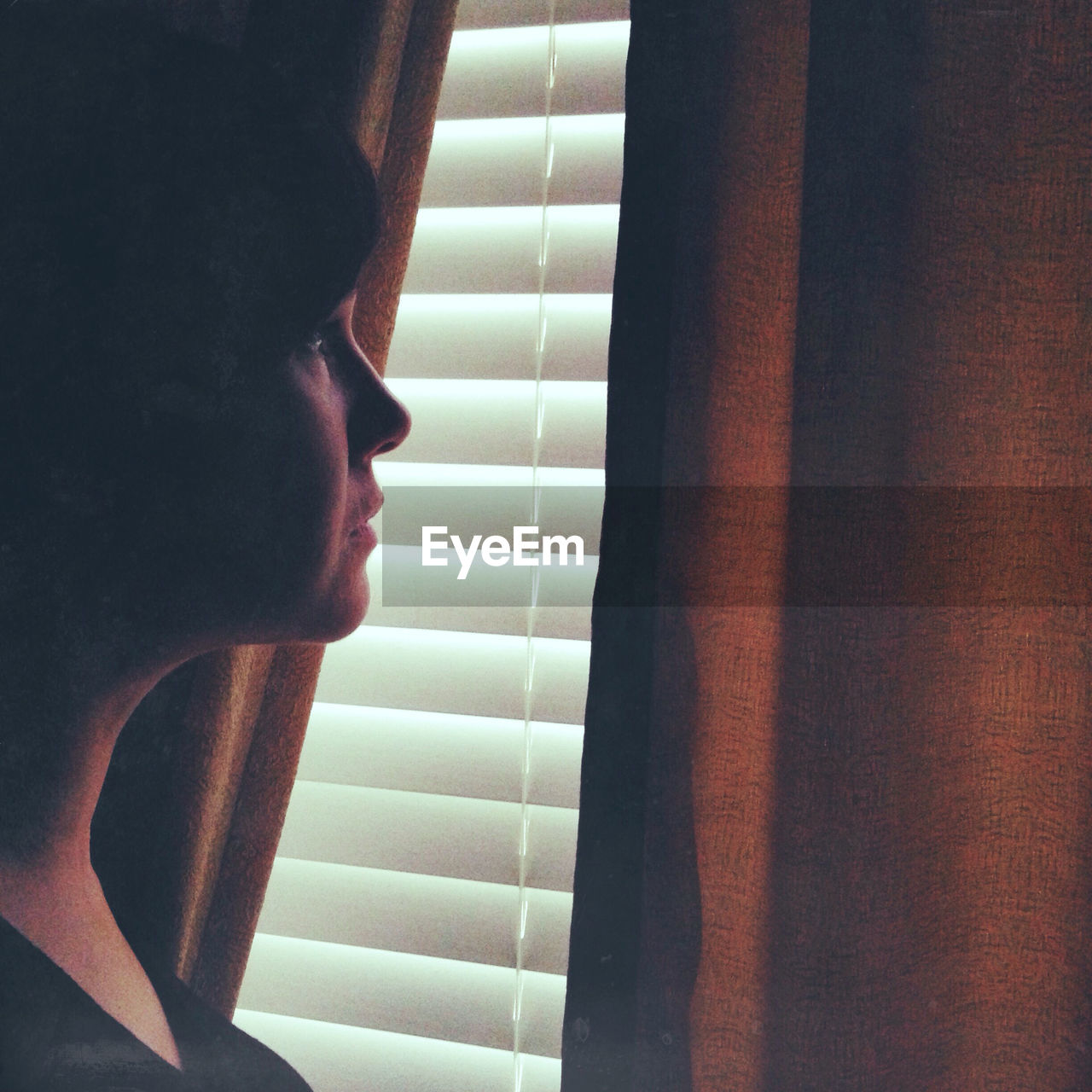 Young woman looking towards blinds at home