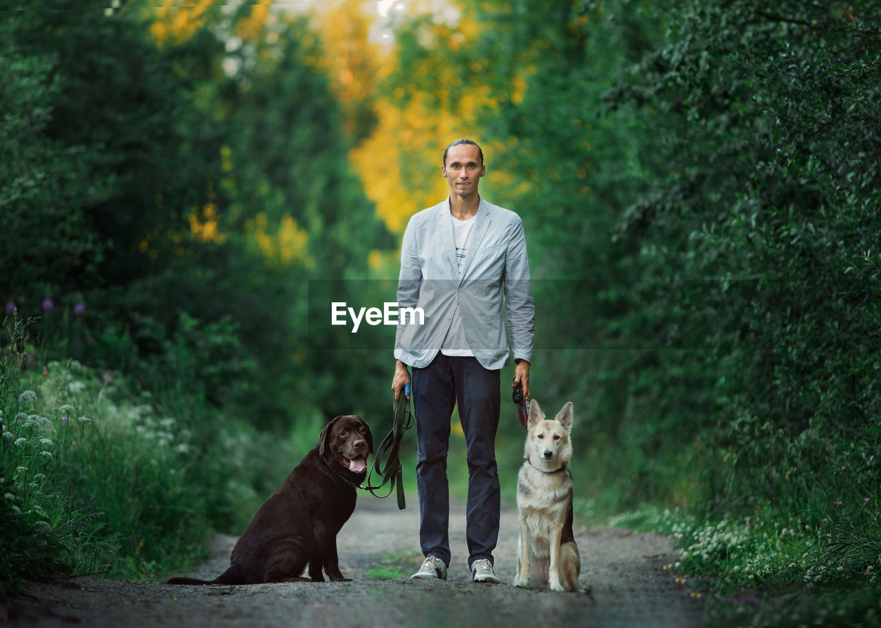 Portrait man standing with of dogs against trees