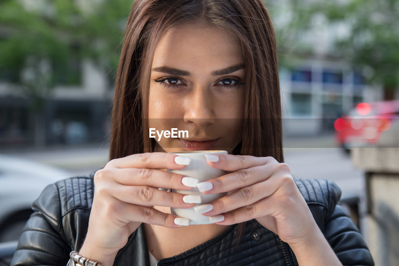 Close-up portrait of young woman drinking coffee at sidewalk cafe