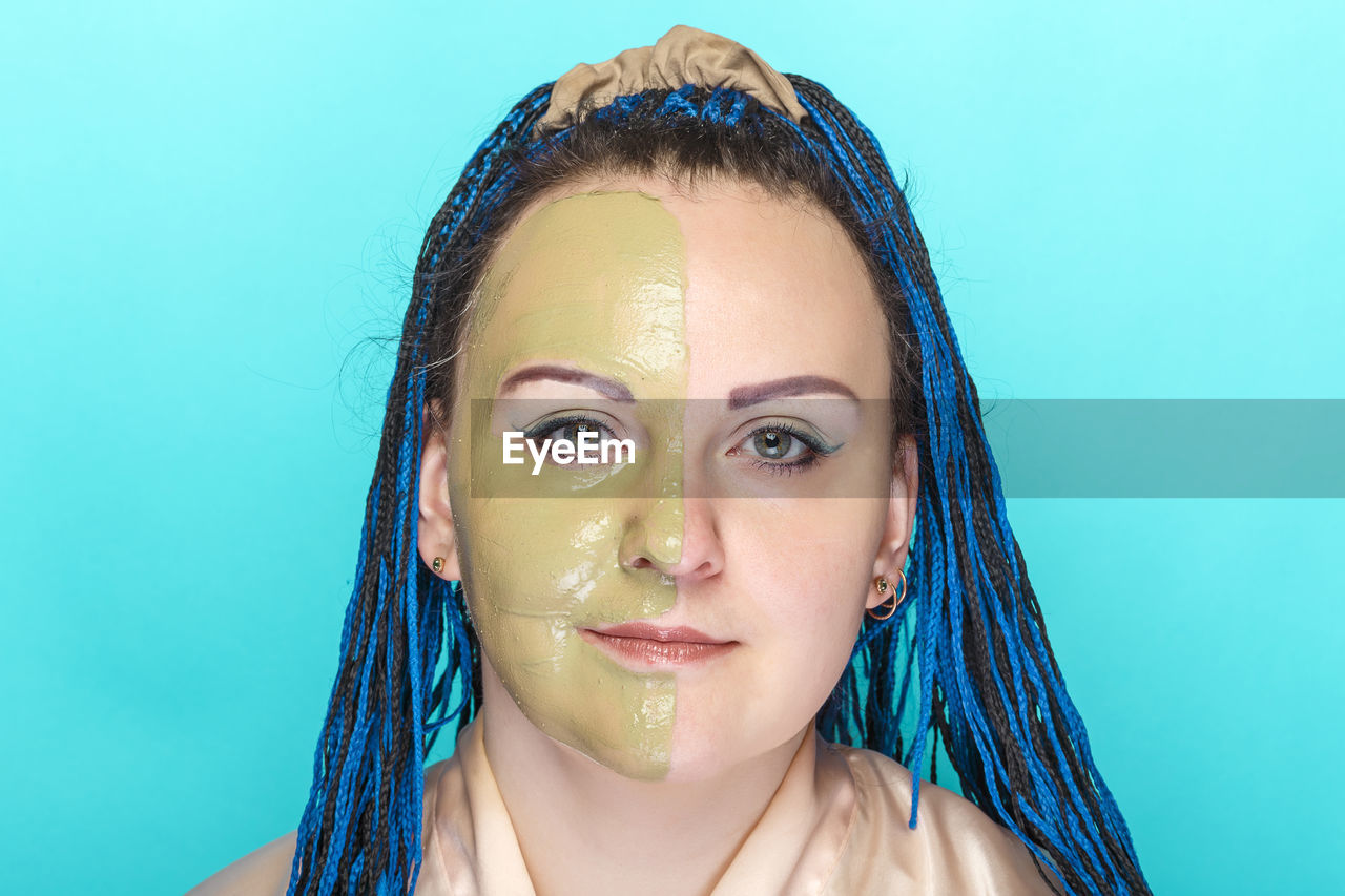 Woman half face in a mask of green clay on a blue background. horizontal photo