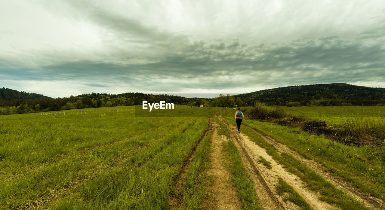 Panorama of a person with backpack hiking in meadow field in countryside on a way to lubon wielki