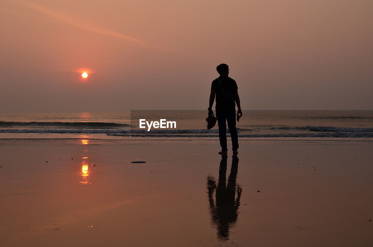 REAR VIEW OF MAN AT BEACH DURING SUNSET