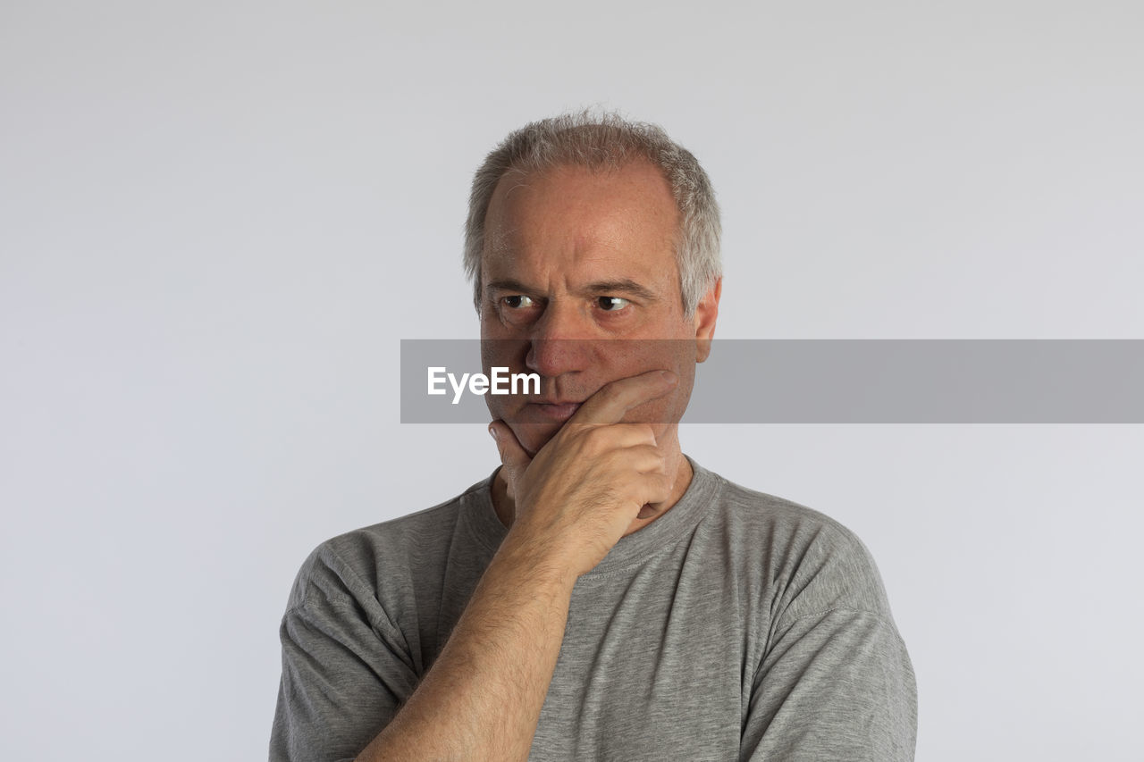 Thoughtful caucasian mature adult, serious facial expression, looks away, keeps fingers on his chin