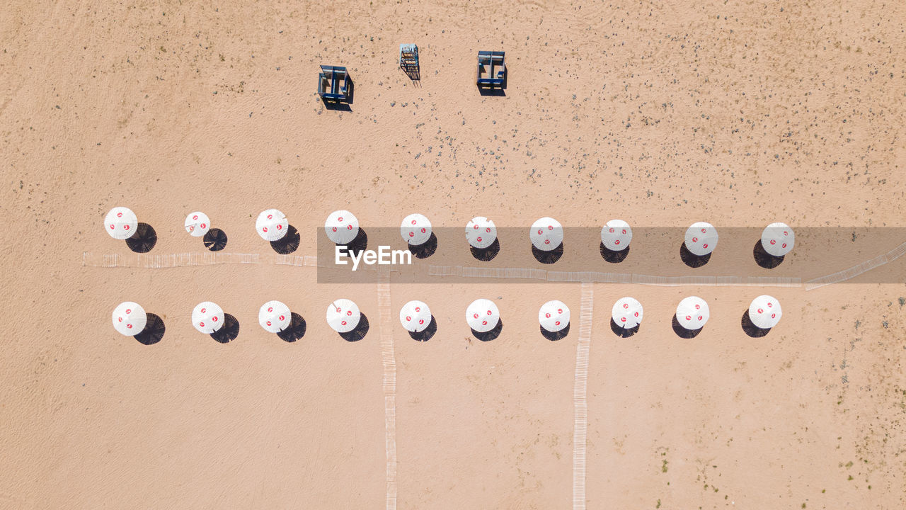 An empty clean sandy beach with two rows of parasols and cabanas, aerial view. 