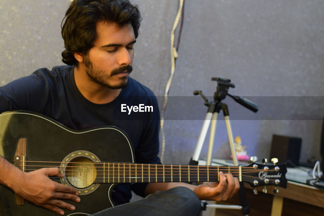 YOUNG MAN PLAYING GUITAR AT CAMERA