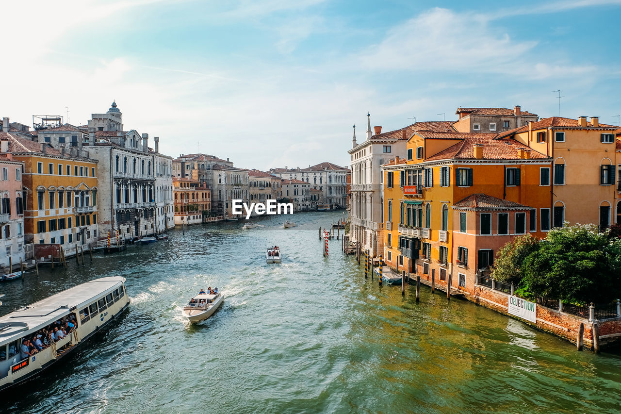 BOATS IN CANAL AMIDST BUILDINGS AGAINST SKY