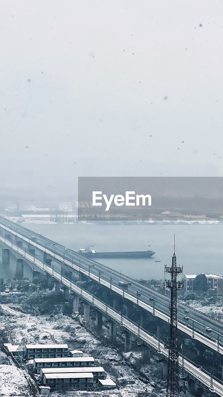 snow, transportation, winter, architecture, sky, nature, built structure, no people, water, cold temperature, transport, horizon, day, city, bridge, sea, travel, high angle view, outdoors, environment, rail transportation, mode of transportation, road, building exterior, track, copy space, travel destinations, vehicle, beauty in nature, scenics - nature, fog, landscape, pier, railroad track