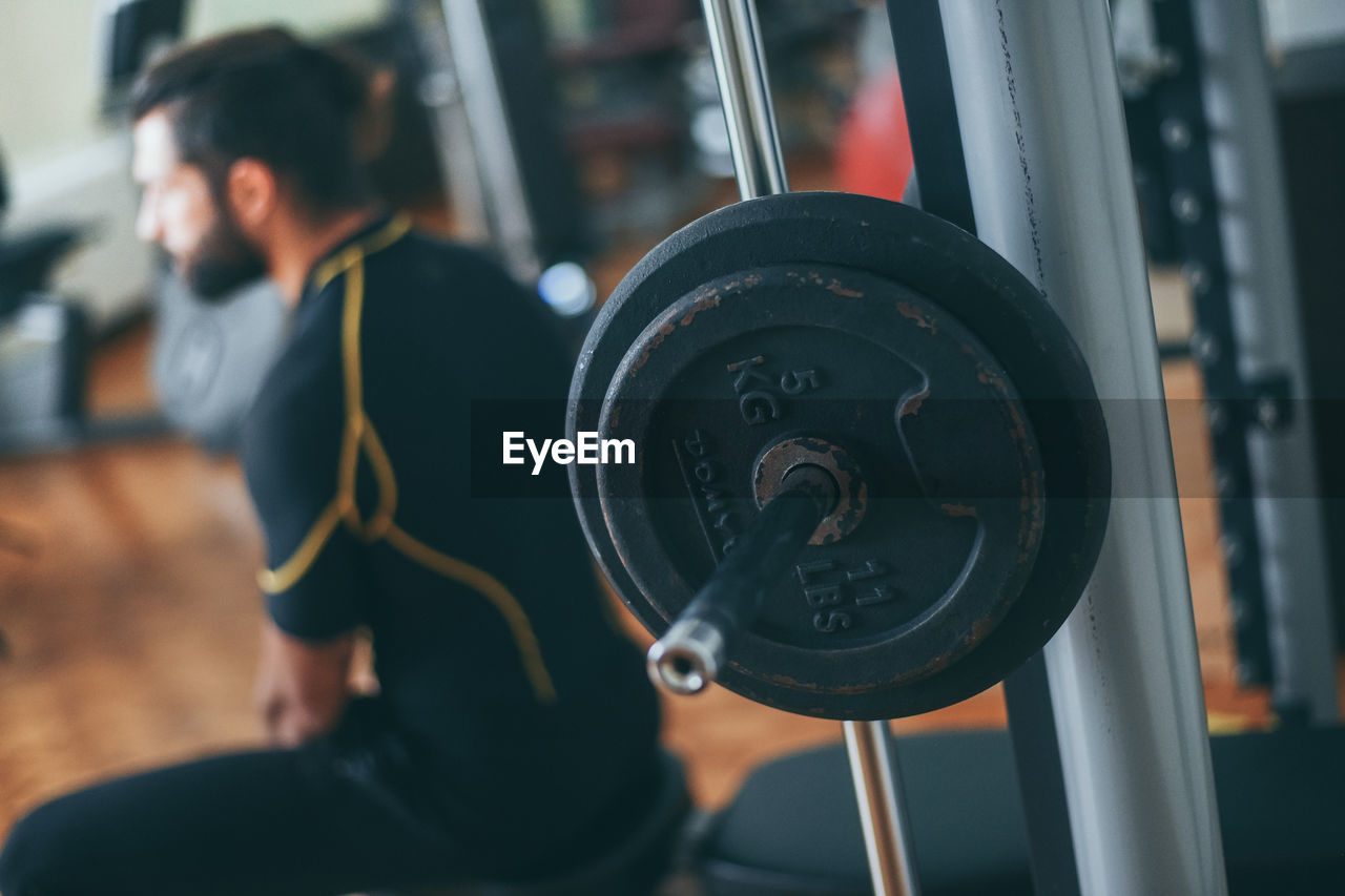 Close up view of a weight in the gym. man athlete in background. closeup of a barbell for fitness