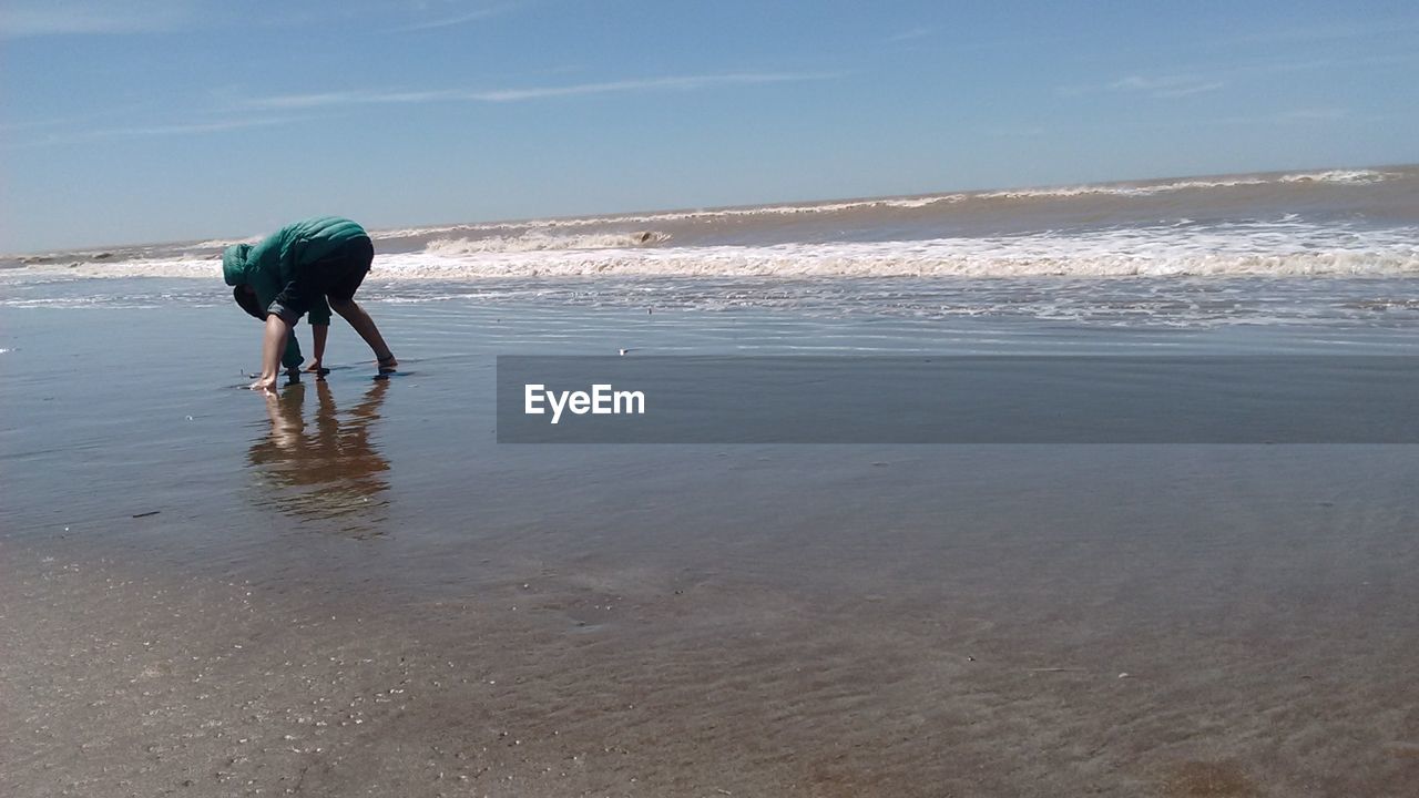 REAR VIEW OF MAN WALKING AT BEACH