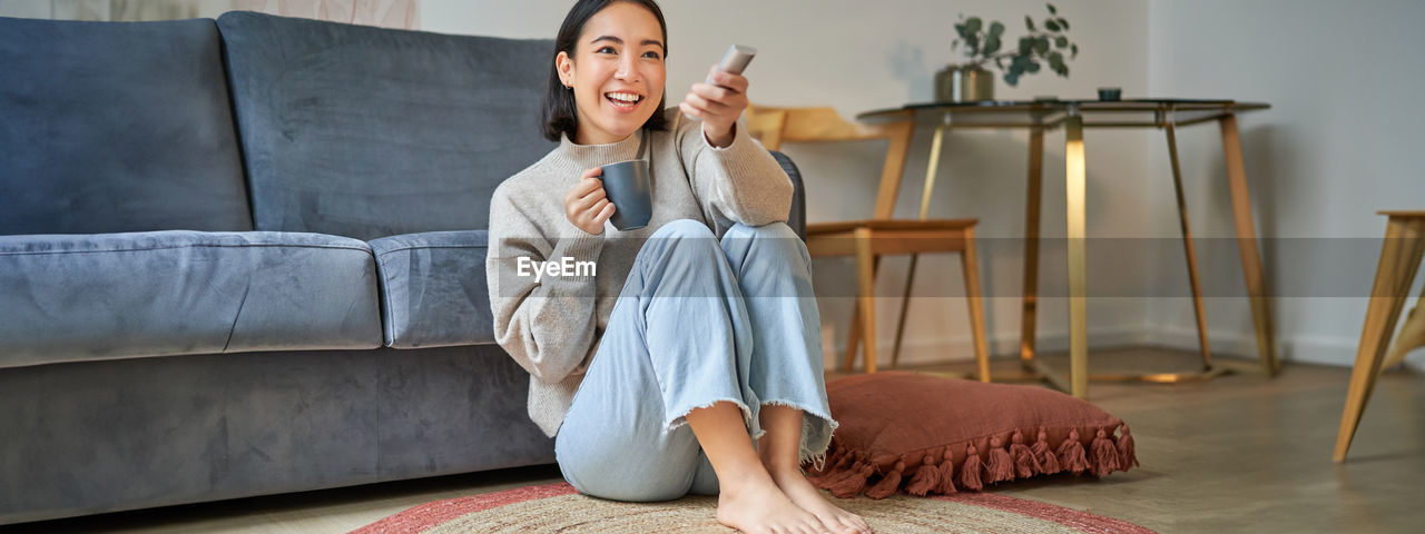 portrait of young woman using mobile phone while sitting on sofa at home